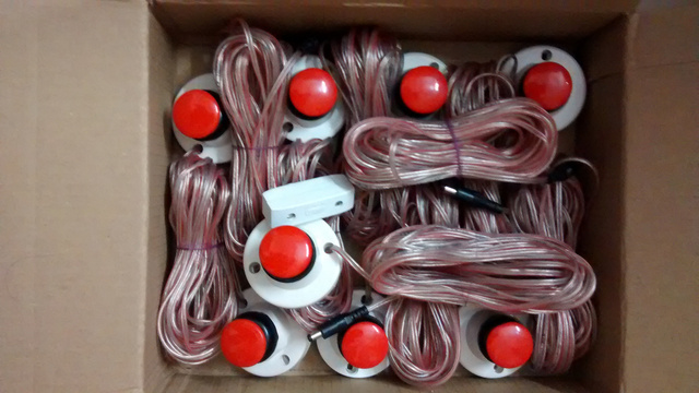 8 big red switches and a door bell switch packed into a cardboard box. A wire with a DC connector is connected to each switch.