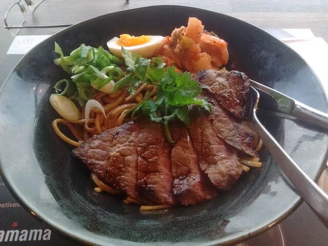 Beef steak, noodles, half a boiled egg and some herbs served on a plate